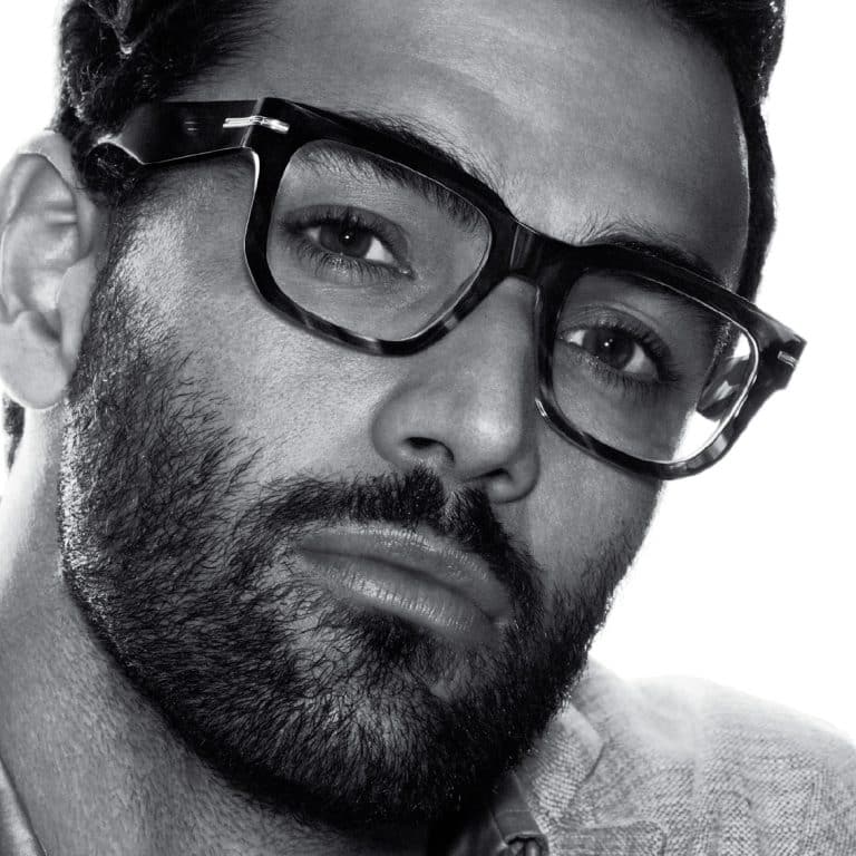 תמונה בשחור-לבן מקרוב של גבר עם זקן ומשקפיים, המביט ישירות למצלמה.